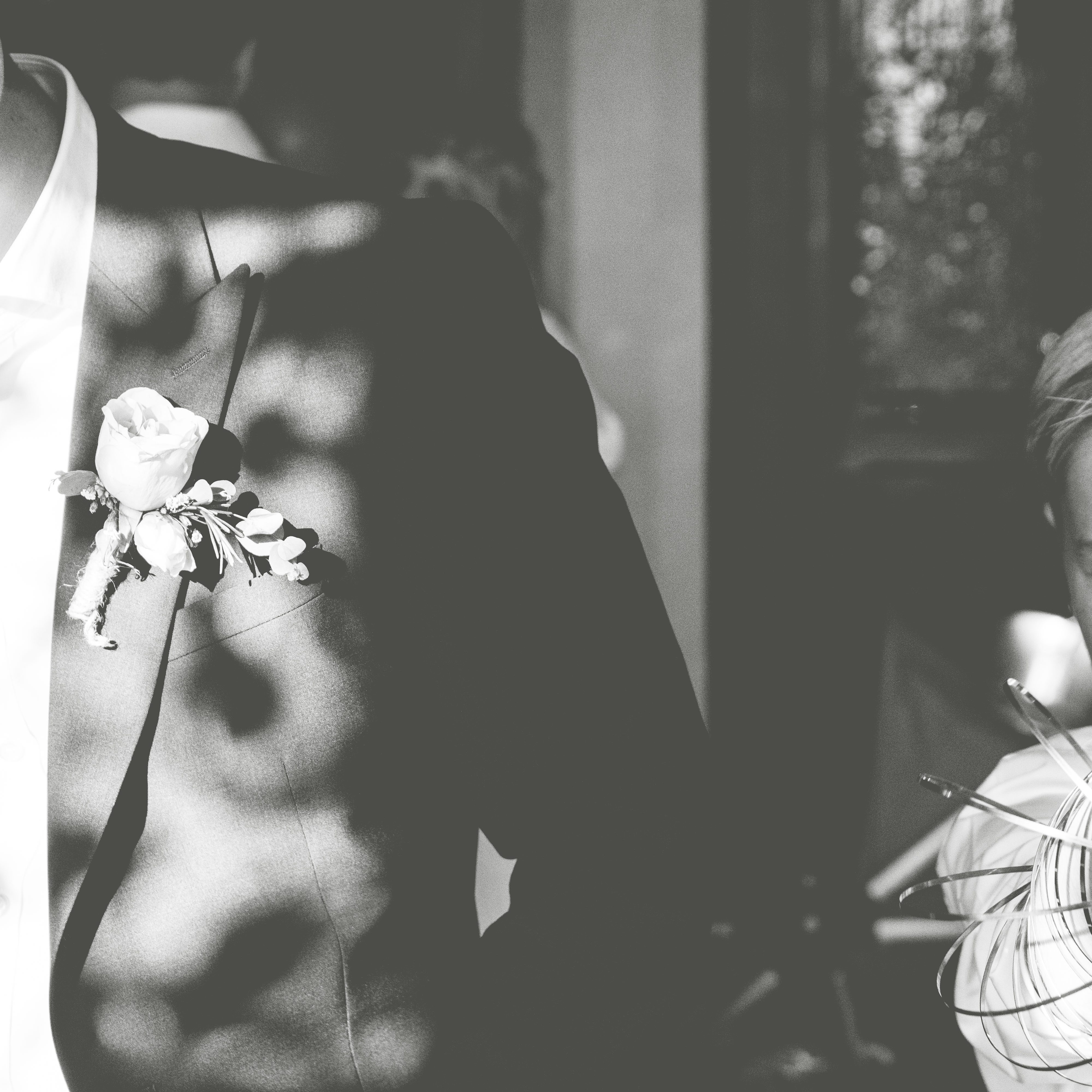 Black and white image of a wedding suit with sun dappling over a boutonniere 