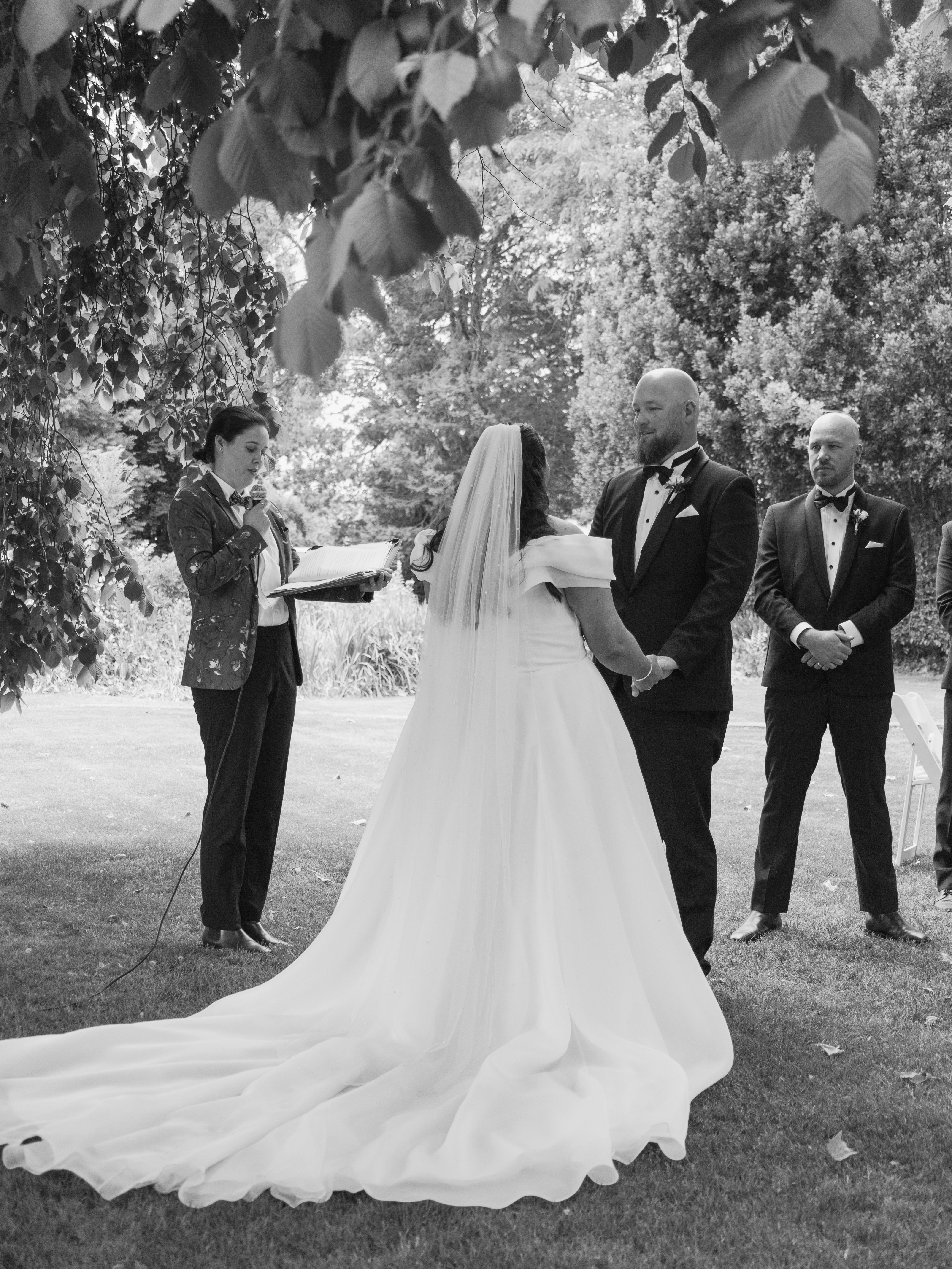 A black and white wedding photo by Studio LJ, showing SJF Celebrant officiate a wedding with a bride and groom