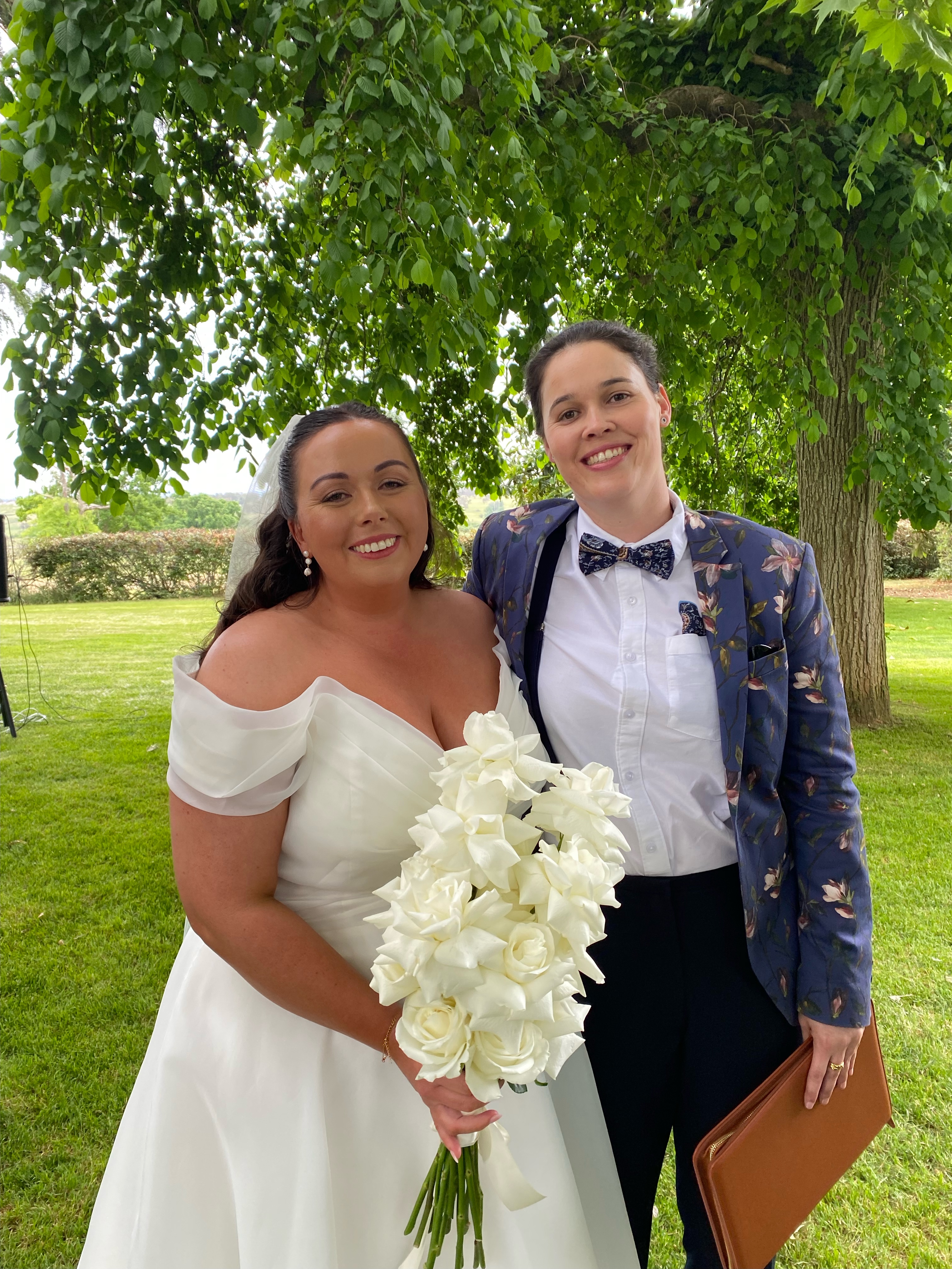Image of SJF Celebrant wearing a blue floral jacket and bowtie, smiling with a beautiful bride
